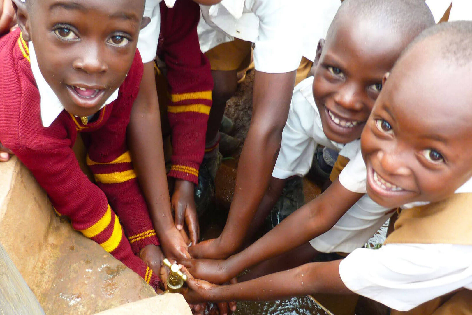 Children smiling while washing their hands on a water tap