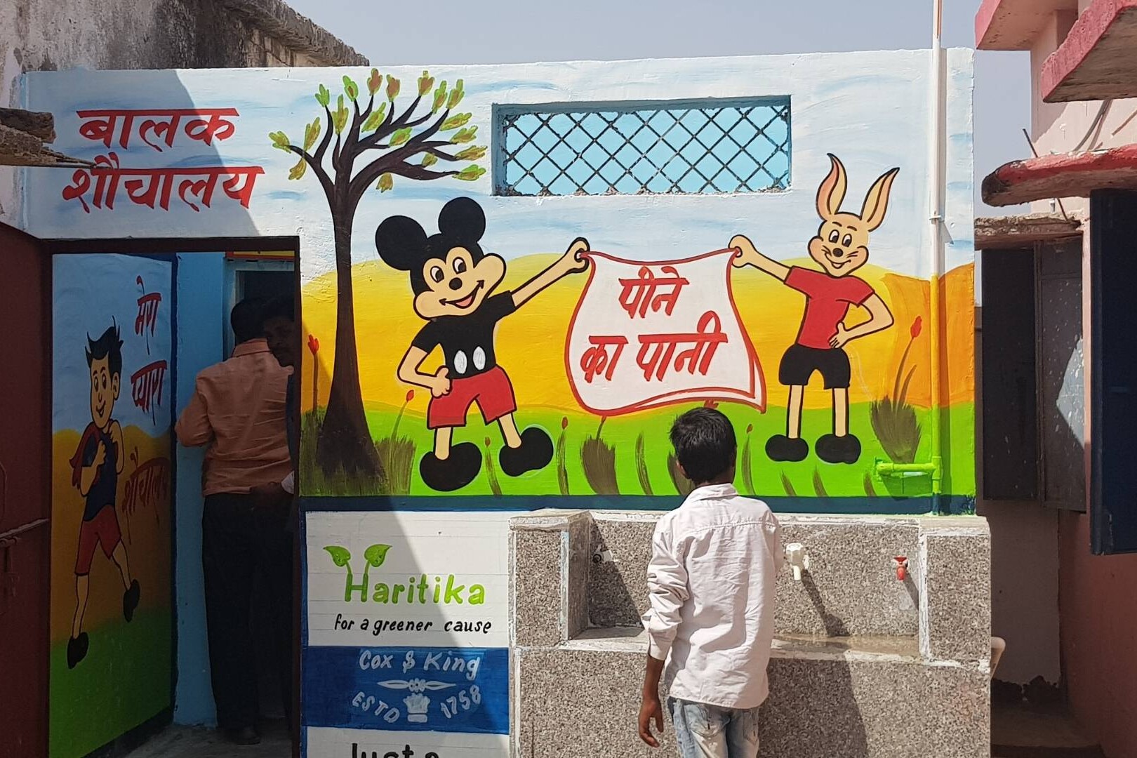 boy washes hands at handwashing station with hygiene mural