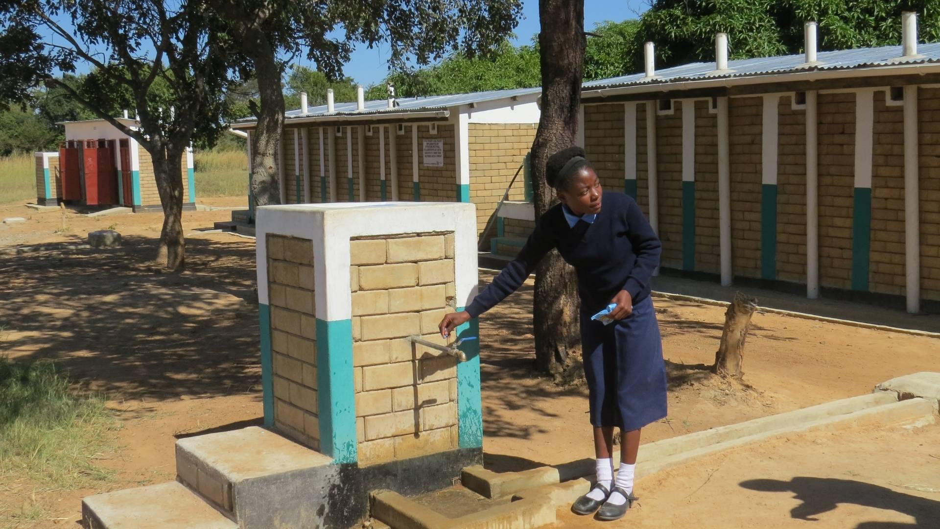 female school student runs tap outside latrine block