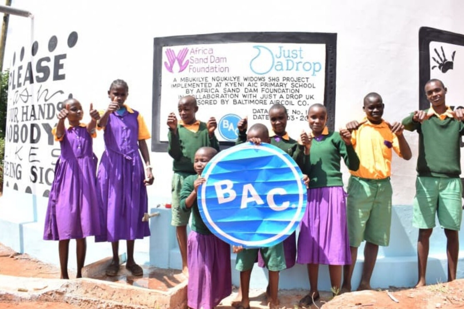 school students by water tank holding bac sign