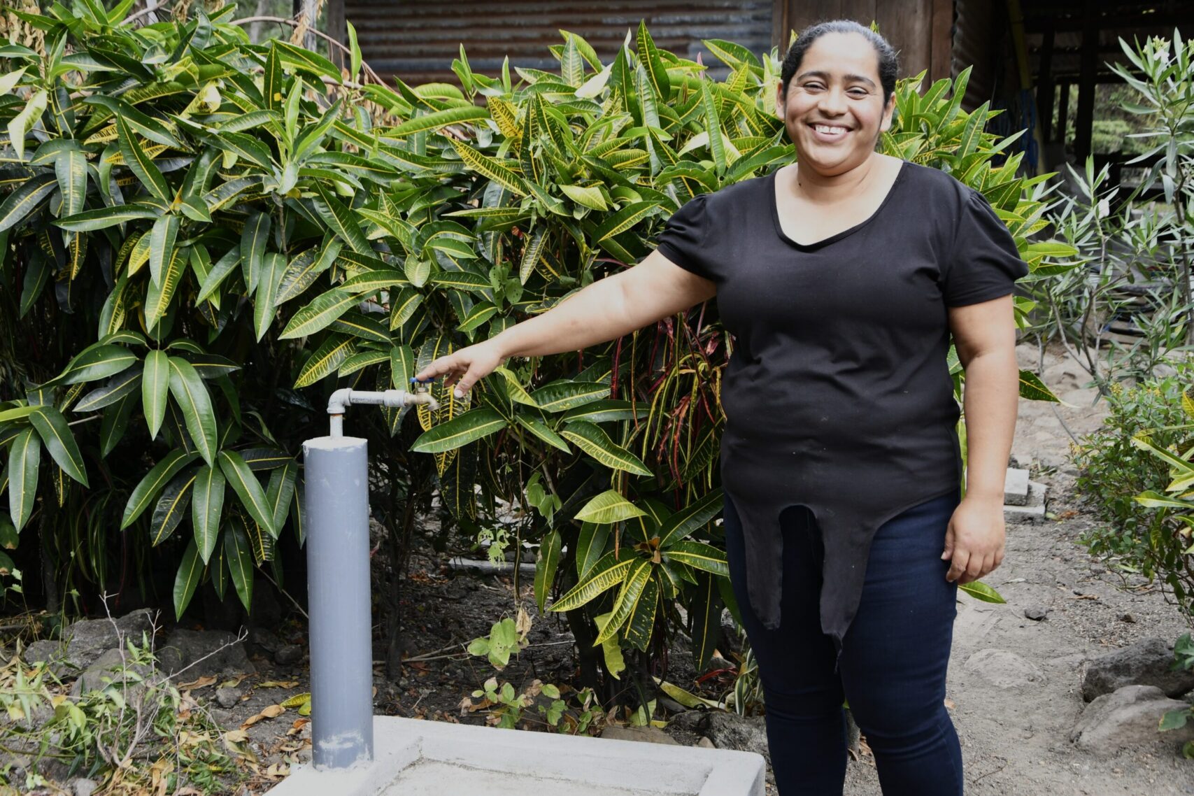 A smiling woman stands next to a water tap