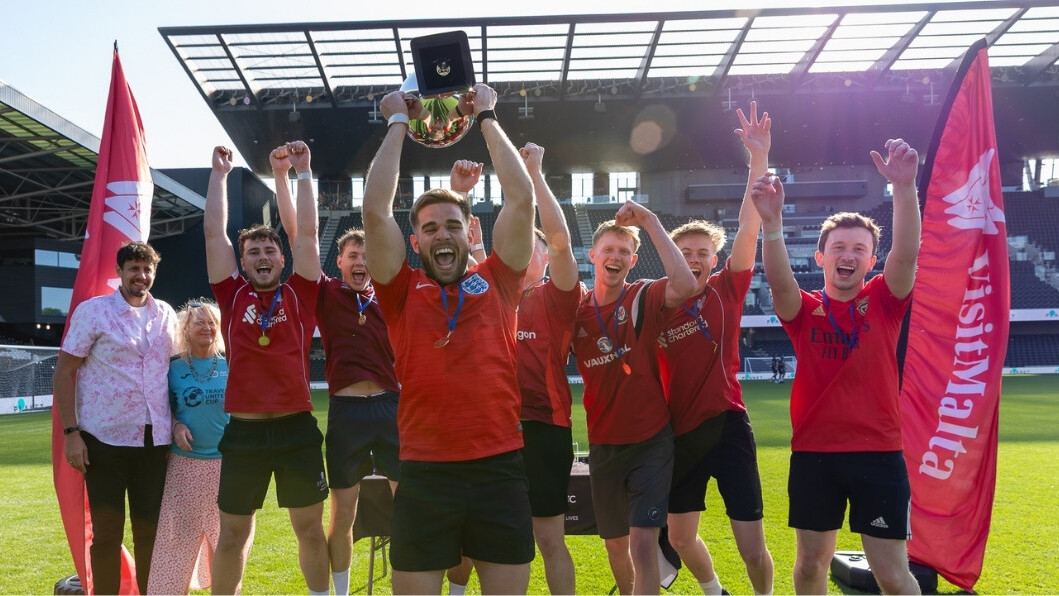 A group of men in red football tops jump into the air. The man at the front is holding a trophy